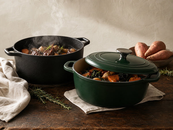 Black cast iron Dutch oven and forest-green enamelled French oven on a timber kitchen bench