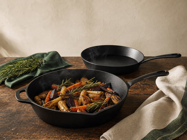 Seasoned cast iron skillets with roasted vegetables on a dark timber kitchen bench